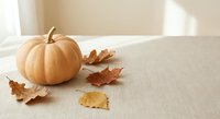 Pale pumpkin and dry autumn leaves on a linen surface in soft natural light, cozy fall seasonal decor concept with copy space.