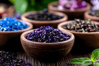 Dried flower petals and herbs in wooden bowls on rustic table, aromatic botanical collection for tea, aromatherapy and natural wellness spa treatments.