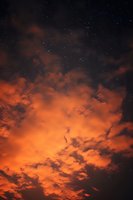 Dramatic orange sunset clouds against dark sky with twinkling stars creating mystical atmosphere for backgrounds and nature photography.
