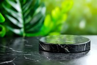 Black marble podium display stand with tropical green leaves background for natural cosmetic product presentation and eco-friendly branding showcase.
