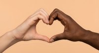Two diverse hands forming heart shape symbol representing unity love friendship and racial harmony on peach background for social campaigns.