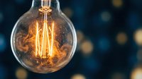 Vintage incandescent light bulb with glowing filament against dark blue bokeh background, suitable for energy, electricity, innovation, and retro design projects.
