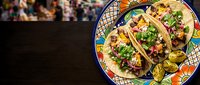 Overhead view of three seasoned tacos with fresh cilantro and diced onions served on a colorful ceramic plate with lime wedges, perfect for food blogs, restaurant menus, and culinary content.