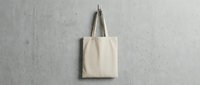 Blank beige cotton tote bag hanging on concrete wall mockup for branding and promotional merchandise design projects.