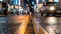 Wet asphalt street with yellow line at night reflecting city lights and blurred traffic in urban downtown area creating atmospheric bokeh effect.