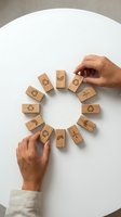 Hands arranging wooden blocks with eco symbols in circle formation on white table representing sustainable business practices and environmental responsibility.