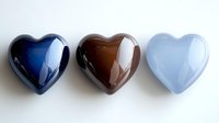 Three glossy heart-shaped stones in navy blue, chocolate brown, and pale blue arranged in a row on white background.