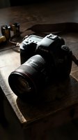 Professional DSLR camera with telephoto lens on wooden surface, studio lighting setup with batteries and equipment for photography professionals and creatives.