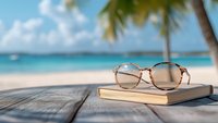 Sunglasses and book on wooden deck overlooking tropical beach with palm trees and turquoise ocean waters. Summer vacation relaxation concept.
