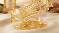 Golden liquid pouring onto surface creating splash and ripple effect, suitable for cosmetics, skincare, wellness and beauty product marketing materials.