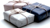Elegantly wrapped gift boxes in white, navy blue, and light pink with simple twine bows arranged on white background for holiday or celebration presentation.