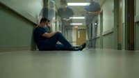Exhausted male healthcare worker in scrubs sitting on hospital floor during break, medical staff burnout and mental health in clinical setting.