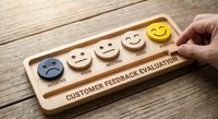 Hand placing wooden token on customer feedback evaluation board with emoji faces from negative to positive rating scale on rustic wood surface.