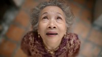 Elderly Asian woman with gray curly hair looking up with hopeful expression, wearing burgundy sweater. Senior citizen portrait for healthcare concepts.