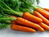 Fresh organic carrots with green tops lying on white surface, macro view showing vibrant orange color and natural texture for healthy eating concept.