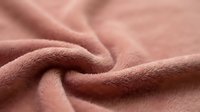 Soft coral pink fleece fabric with gentle folds and texture, cozy material for blankets, clothing and home decor projects.