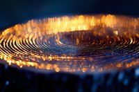 Glowing spiral pattern with orange light reflections on metallic surface creates dramatic abstract background with bokeh effect in dark environment.