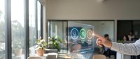 Young professional man pointing at digital interface with business analytics icons on glass screen in modern office environment with colleagues in background.