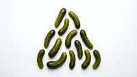 Pickled gherkins arranged in a smiley face pattern on white background, fresh fermented cucumbers for food styling, cooking, recipes, and culinary design projects.