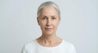 Senior Caucasian woman with gray hair wearing white top against neutral background, mature female portrait for healthcare and lifestyle concepts.