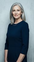 Confident mature businesswoman with gray hair in navy dress smiling at camera against concrete wall background for corporate and professional use.