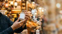 Cropped view of male hands holding blank white box against warm-lit retail store interior with bokeh background, suitable for product packaging mockups and commercial advertising.