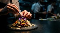 Professional chef plating gourmet dish with tweezers in upscale restaurant kitchen, fine dining culinary artistry and food presentation techniques.