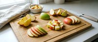 Fresh apple slices and cheese cubes arranged on wooden cutting board in bright kitchen setting for healthy snacking and food preparation.