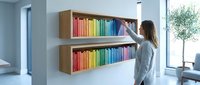 Young woman reaching for colorful books on modern floating wooden shelves in bright contemporary home library interior for organization and learning.