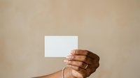 Close-up of hand holding blank white card against neutral beige background, suitable for business cards, promotional materials, and marketing campaigns.