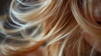Close-up of blonde hair strands with soft waves and highlights creating a textured pattern against blurred background, suitable for beauty and haircare advertising.