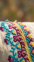 Colorful hand embroidered textile with vibrant floral patterns in turquoise, pink and yellow threads on natural linen fabric for traditional crafts and decor.