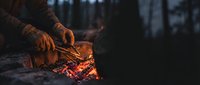 Hands warming over glowing campfire embers in dark forest setting, outdoor survival and wilderness camping adventure concept.
