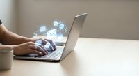 Professional woman typing on laptop with digital communication icons floating above keyboard representing modern business connectivity and online networking.