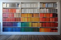 Rainbow colored books arranged on white wooden shelves creating spectrum pattern from blue to red. Modern library interior with hardwood flooring and organized literature.