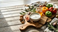 Fresh Mediterranean appetizer platter with creamy dip, crackers, colorful tomatoes, nuts and herbs on rustic wooden board for entertaining.