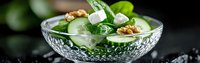 Fresh green salad with cucumber, feta cheese, walnuts and herbs in crystal bowl. Healthy Mediterranean diet meal for restaurant menu or cooking blog.