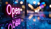 Glowing pink neon open sign reflected on wet surface with blurred city lights and bokeh in background creates atmospheric nighttime urban scene.