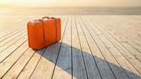 Vintage orange suitcase standing on a wooden pier at sunset, casting a long shadow, evoking travel, adventure, and nostalgia.