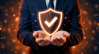 Businessman in suit holding glowing shield with checkmark symbol representing cybersecurity, data protection and business insurance concepts.