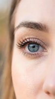 Close-up of woman's blue eye with natural makeup and long eyelashes showing detailed iris and eyebrow for beauty and cosmetic concepts.