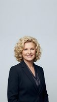 Professional mature blonde businesswoman in dark suit smiling confidently against neutral background for corporate marketing materials.