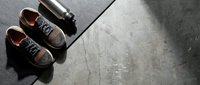 Pair of brown work boots with orange accents and metal thermos on dark concrete surface, overhead flat lay composition for footwear and industrial lifestyle content.