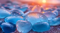 Translucent blue sea glass pebbles with water drops against sunset background, creating dreamy bokeh effect and magical atmosphere for wellness and spa designs.