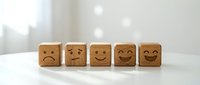 Five wooden blocks with carved emoji faces showing emotions from sad to happy on white surface, representing customer satisfaction and feedback scale.