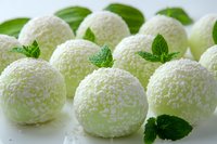 White coconut candy balls decorated with fresh mint leaves on light background. Sweet homemade dessert truffles rolled in shredded coconut flakes.