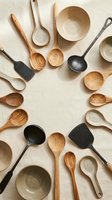 Wooden kitchen utensils and ceramic bowls arranged in circle on beige background. Natural cooking tools for culinary preparation and food styling.