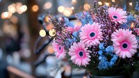 Pink gerbera daisies and blue delphinium flowers arranged in romantic bouquet with soft bokeh lights creating dreamy atmosphere in background.
