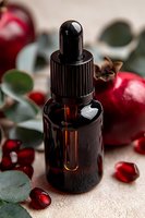 Amber glass dropper bottle with essential oil surrounded by fresh pomegranate seeds, eucalyptus leaves and natural ingredients on beige background.