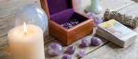 Spiritual wellness setup with burning candle, amethyst crystals, tarot cards and wooden box on rustic table for meditation and divination practices.